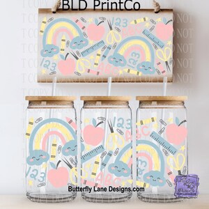 May include: Three clear glass tumblers with bamboo lids and straws, decorated with a school-themed design. The design includes rainbows, apples, scissors, rulers, and the text "123" and "ABC". A wooden sign above repeats the design. The text "BLD PrintCo" and "Butterfly Lane Designs.com" are also visible.