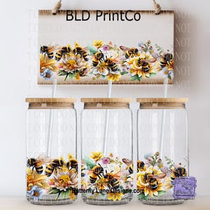 May include: Three clear glass tumblers with bamboo lids and straws, decorated with a bee and floral design. A wooden sign above reads "BLD PrintCo" and features the same bee and floral pattern. The website "Butterfly Lane Designs.com" is also visible.