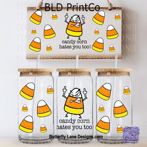 May include: Three clear glass tumblers with bamboo lids and straws, decorated with candy corn graphics and the phrase "candy corn hates you too!". A wooden sign with the same design hangs above. The design includes an angry candy corn character.