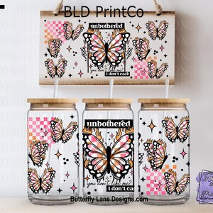 May include: Clear glass beverage cups with bamboo lids, featuring a butterfly design with the words "unbothered" and "you don't like me? I don't care." The design includes pink, orange, and black butterflies and stars. A wooden sign with the same design hangs above.