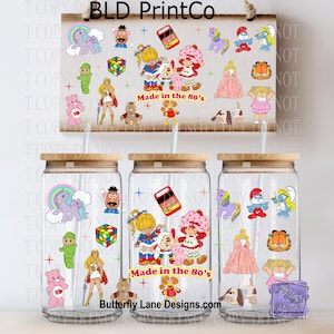May include: Three clear glass tumblers with bamboo lids and straws, featuring colorful 1980s cartoon character decals including a unicorn, Rubik's cube, Strawberry Shortcake, and Garfield. The text Made in the 80's is printed on each glass.