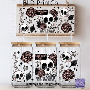 May include: Three glass tumblers with bamboo lids and straws, decorated with skulls, roses, stars, and the text "may we all heal from the things we don't talk about." A matching wooden sign hangs above.