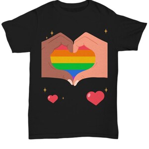 May include: Black t-shirt featuring a heart made of hands, with a rainbow-colored heart in the center. Two red hearts and gold stars are also on the shirt. The design promotes love and inclusivity.