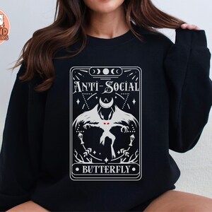 Könnte beinhalten: Schwarzer Pullover mit einem weißen Grafikdruck einer Tarotkarte. Die Karte zeigt einen weißen Schmetterling mit roten Augen und den Text "Anti-Social Butterfly".