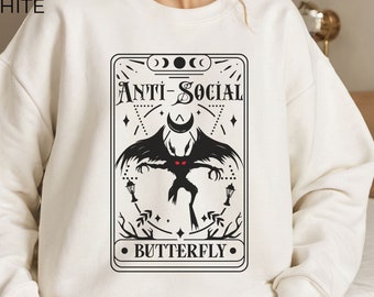 Puede incluir: Sudadera blanca con un estampado gráfico en blanco y negro de una criatura con alas y el texto "Anti-Social Butterfly".