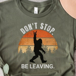 K&ouml;nnte beinhalten: Gr&uuml;nes T-Shirt mit einer Retro-Grafik von Bigfoot mit dem Text "Don't Stop. Be Leaving."