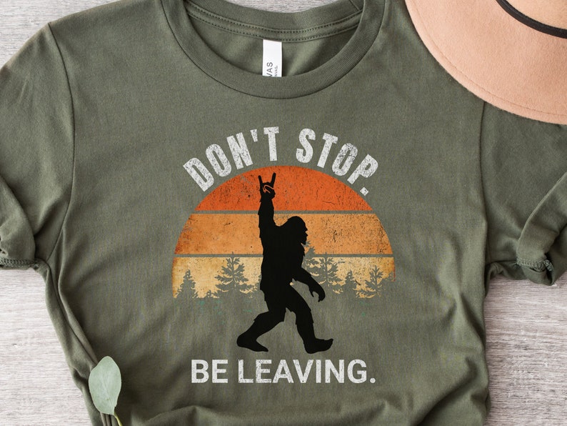 K&ouml;nnte beinhalten: Gr&uuml;nes T-Shirt mit einer Retro-Grafik von Bigfoot mit dem Text "Don't Stop. Be Leaving."
