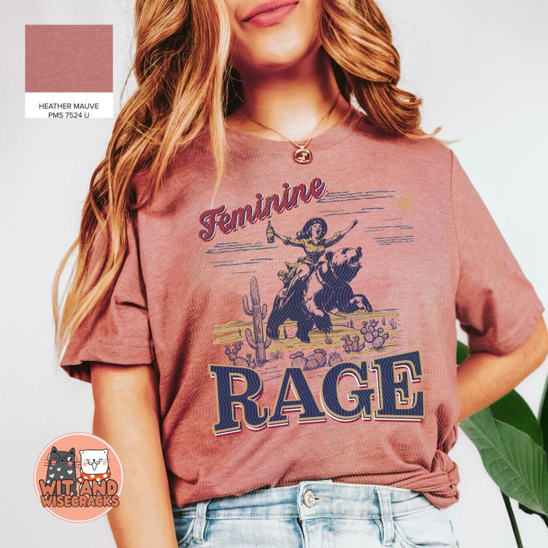 May include: A heather mauve t-shirt with a graphic of a woman riding a bear and the text "Feminine Rage".