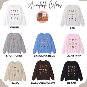 May include: A graphic design of two cats with the text "Wit and Wisecracks" in a circle. The image is displayed on a variety of sweatshirts in different colors, including white, ash, sport grey, carolina blue, light pink, sand, dark chocolate, and black.