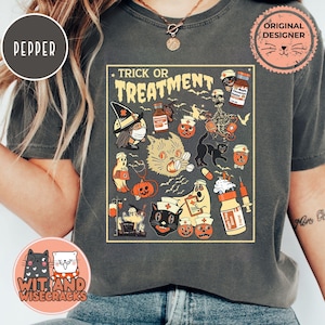 May include: Dark gray t-shirt featuring a Halloween-themed graphic with the words "Trick or Treatment." The design includes a witch, cat, skeleton, pumpkins, and medical supplies. The shirt has a round neckline and short sleeves.