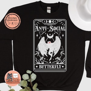 Könnte beinhalten: Schwarzer Pullover mit einer weißen Grafik einer geflügelten Kreatur und dem Text "Anti-Social Butterfly".