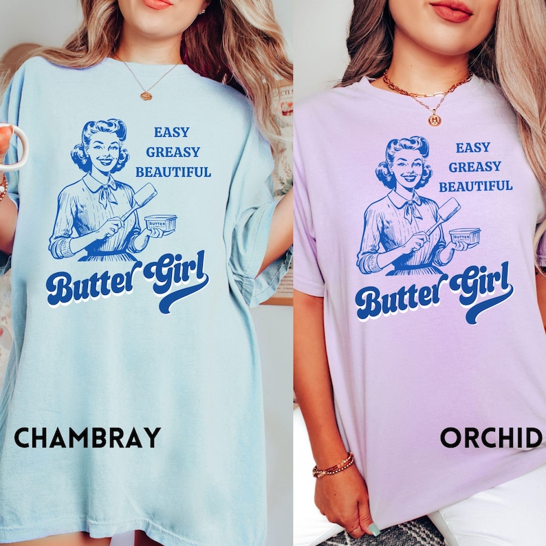 Pode incluir: Duas camisetas com uma ilustra&ccedil;&atilde;o retr&ocirc; de uma mulher segurando uma esp&aacute;tula e um recipiente de manteiga. O texto nas camisetas diz "Easy Greasy Beautiful Butter Girl". As camisetas est&atilde;o dispon&iacute;veis em Chambray e Orchid.