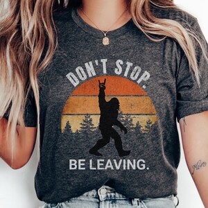 K&ouml;nnte beinhalten: Graues T-Shirt mit einer Grafik im Vintage-Stil einer Bigfoot-Figur mit dem Text "Don't Stop. Be Leaving."