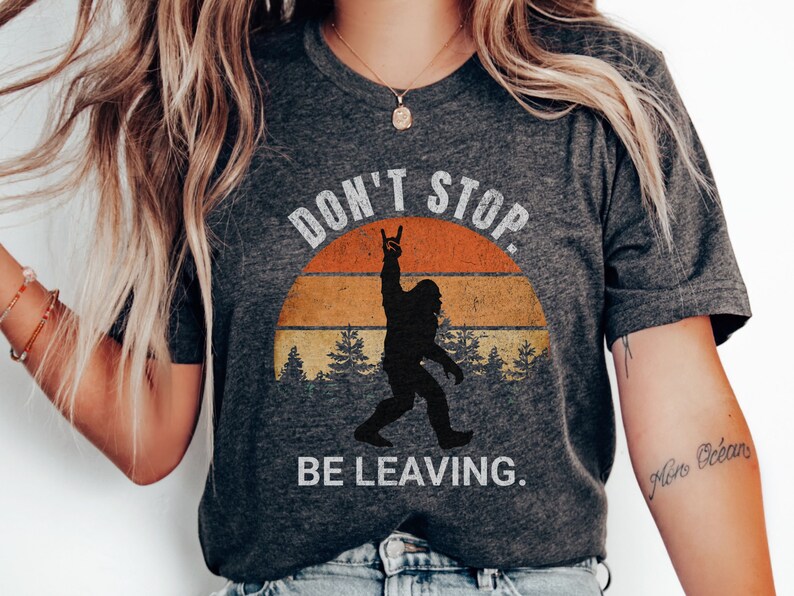 K&ouml;nnte beinhalten: Graues T-Shirt mit einer Grafik im Vintage-Stil einer Bigfoot-Figur mit dem Text "Don't Stop. Be Leaving."