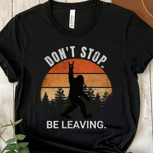 May include: Black t-shirt with a retro sunset graphic and a silhouette of Bigfoot with the text "Don't Stop. Be Leaving."