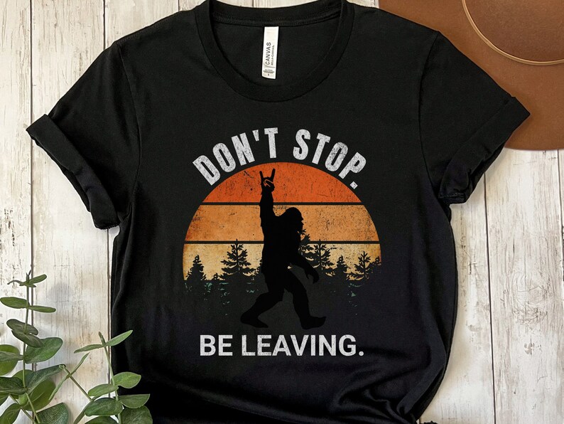 May include: Black t-shirt with a retro sunset graphic and a silhouette of Bigfoot with the text "Don't Stop. Be Leaving."