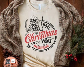 May include: A beige t-shirt with a graphic design of a cartoon character with the text "Have the Christmas You Deserve".