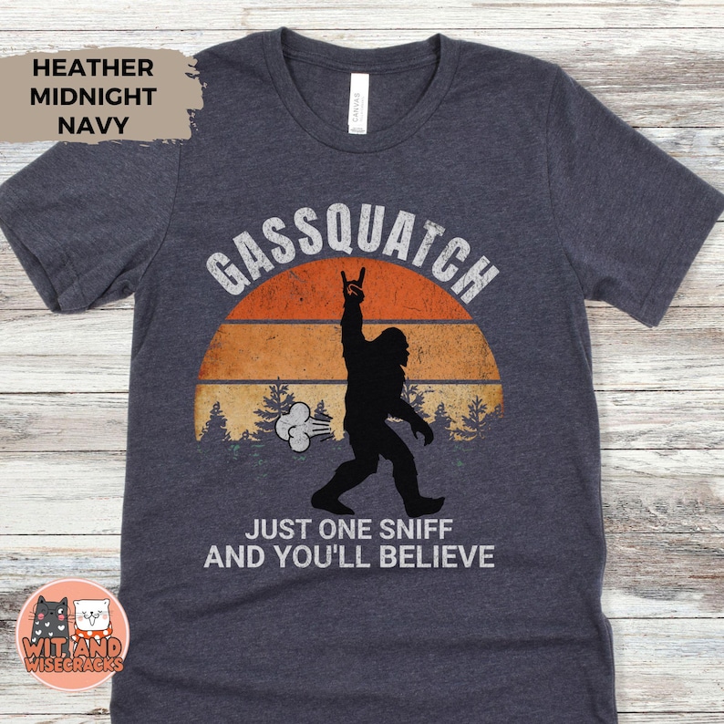 May include: Heather midnight navy t-shirt with a graphic of a Bigfoot silhouette giving a rock-on hand gesture in front of a sunset. Text reads "Gassquatch" and "Just one sniff and you'll believe."