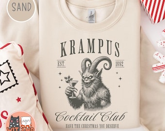 Puede incluir: Una sudadera beige con una ilustración en blanco y negro de un monstruo sosteniendo una copa de cóctel. El texto "KRAMPUS Cocktail Club EST. 1692 HAVE THE CHRISTMAS YOU DESERVE" está impreso en la sudadera.