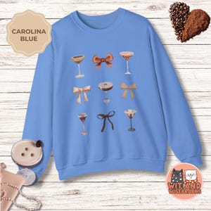 May include: A light blue sweatshirt with a graphic design of various cocktails and bows. The text "CAROLINA BLUE" is in a white box at the top left of the image.