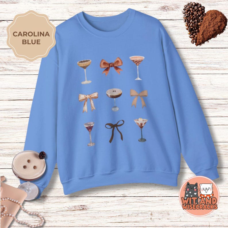 May include: A light blue sweatshirt with a graphic design of various cocktails and bows. The text "CAROLINA BLUE" is in a white box at the top left of the image.