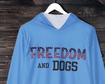 Könnte beinhalten: Ein hellblauer Hoodie mit langen Ärmeln und einer weißen Kapuze. Auf der Vorderseite des Hoodies steht "FREEDOM AND DOGS", wobei das Wort "FREEDOM" in rot-weiß-blauem amerikanischem Flaggenmuster gedruckt ist. Die Ärmel haben ein kleines Pfotenabdruckdesign in rot-weiß-blau.