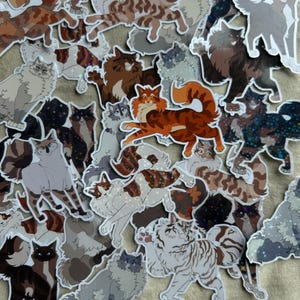 Può includere: Una collezione di adesivi per gatti in vari colori e motivi. Gli adesivi presentano diverse razze e pose di gatti, tra cui gatti calico, tabby e di colore uniforme. Alcuni adesivi hanno accenti glitterati, e il tema generale è stravagante e giocoso.