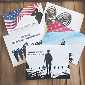May include: A collection of white greeting cards featuring military-themed graphics, including silhouettes of soldiers saluting, a camouflage heart, and American flag motifs. Text includes "I am so very proud of the", "Stay Strong! You are half way through bootcamp!", and "BELIEVE IN YOURSELF LIKE WE BELIEVE IN YOU!"