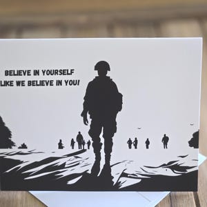 May include: A white greeting card featuring a black silhouette illustration of a soldier standing in the foreground with smaller figures in the background. The text printed on the left side reads, "BELIEVE IN YOURSELF LIKE WE BELIEVE IN YOU!"