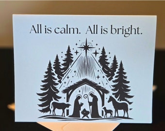 May include: A blue Christmas card with a black silhouette of a nativity scene. The card reads "All is calm. All is bright."