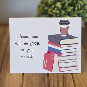 May include: A white greeting card with the text "I know you will do great on your exams!" features a stack of books and a coffee cup. The books are various colors, including red, blue, and gray.