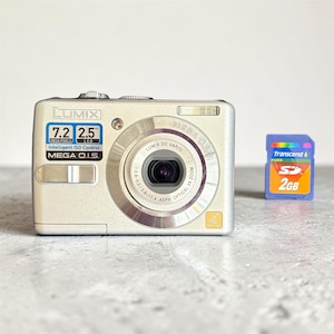 以下が含まれることがあります： 7.2メガピクセルのセンサー、2.5インチの液晶画面、Mega O.I.S.レンズを搭載したシルバーのLumixデジタルカメラと、青いTranscend製2GB SDメモリーカード。Lumix DC Varioレンズは3倍の光学ズーム機能を備えています。