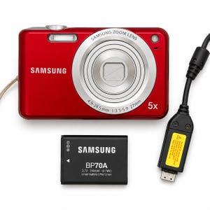 May include: A red Samsung digital camera with a 5x zoom lens, a black BP70A 3.7V 740mAh lithium-ion battery, and a black USB charging cable with a yellow warning label. The camera lens features text reading Samsung Zoom Lens 4.9-24.5 mm 1:3.5-5.9 27mm.