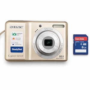 May include: A gold Sony Cyber-shot digital camera with a 3x optical zoom lens, 10.1 megapixels, and features including Intelligent Auto, Smile Shutter, Face Detection, and SteadyShot. Beside the camera is a blue SanDisk 8GB SDHC memory card.