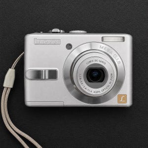 以下が含まれることがあります： シルバーのLumixデジタルカメラ。Lumix DC Varioレンズ（1:2.8-5.0/5.8-17.4 ASPH、光学4倍ズーム）、Mega O.I.S.のロゴ、小型フラッシュを搭載し、コンパクトな長方形の本体側面にはベージュのリストストラップが取り付けられています。