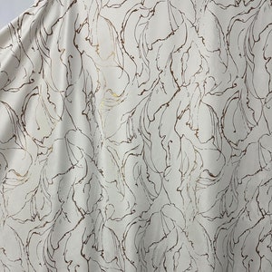May include: White fabric with a brown and gold abstract floral pattern.