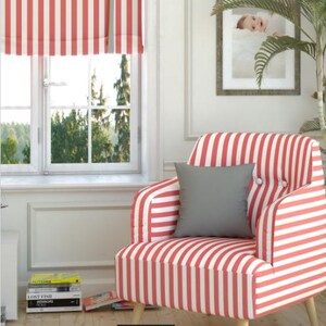 May include: A red and white striped armchair with a gray pillow. The chair has wooden legs and is positioned in front of a window with a matching striped shade. A framed picture and a plant are also visible.