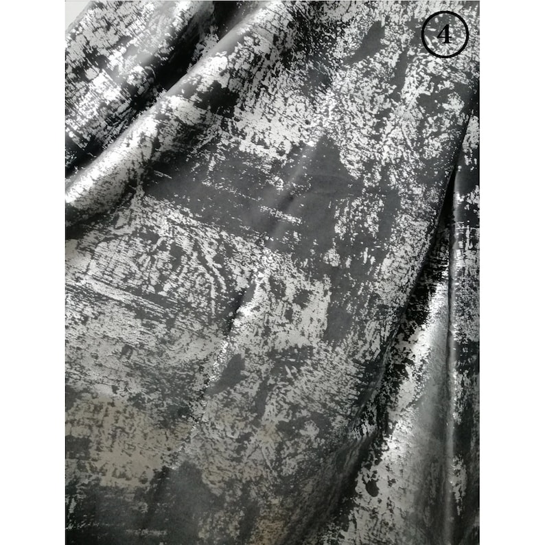 May include: Close-up of a black fabric with a silver metallic finish. The fabric has a textured, distressed look, resembling a brushed or worn surface.