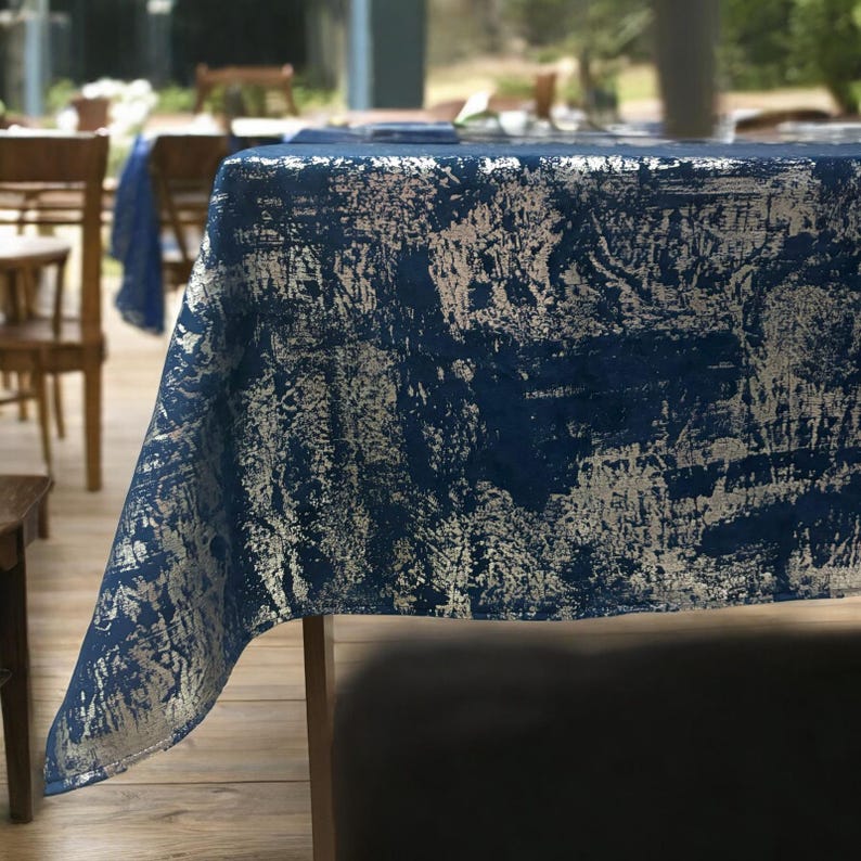 May include: A blue and silver tablecloth with a distressed, abstract pattern. The tablecloth is made of linen and has a soft, textured feel.