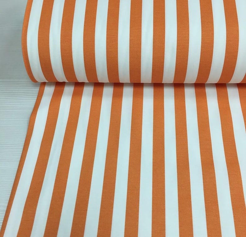 May include: A roll of fabric featuring vertical stripes in orange and white. The stripes are evenly spaced and run the length of the fabric. The fabric is tightly rolled, with the pattern visible on the surface.