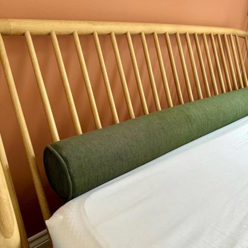 Puede incluir: Una almohada de apoyo verde sobre una cama blanca con una cabecera de madera. La cabecera tiene un dise&ntilde;o de listones.