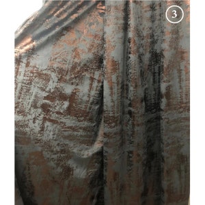 May include: Close-up of a dark gray fabric with a metallic copper-colored abstract pattern. The fabric has a subtle sheen and a textured surface.