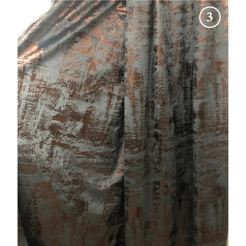 May include: Close-up of a dark gray fabric with a metallic copper-colored abstract pattern. The fabric has a subtle sheen and a textured surface.