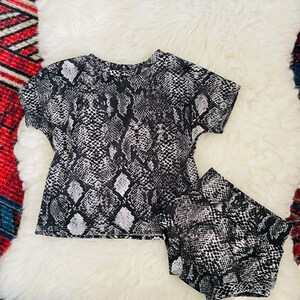 May include: A black and white snake print two-piece set with a short-sleeved top and shorts.
