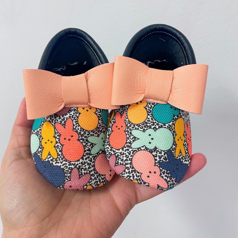 May include: A pair of black canvas shoes with a pink bow and a colorful Peeps marshmallow pattern.
