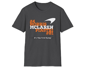 May include: A dark gray t-shirt with a white McLaren logo and orange text that reads "#4 NORRIS MCLAREN PIASTRI #81" and "It's Time To Go Racing!"
