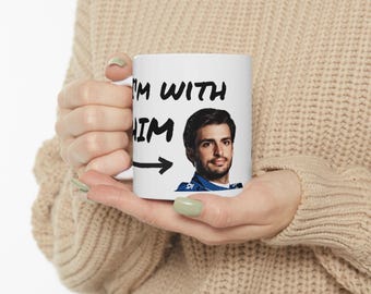 May include: White ceramic mug with black text that reads "I'm with him" and an arrow pointing to the right. A photo of a man in a blue racing suit is to the right of the text.