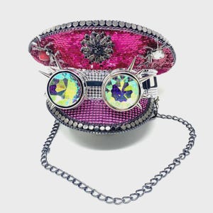 May include: A pink sequined hat with silver trim and a decorative jewel. The hat features iridescent goggles with silver spikes and a silver chain. A decorative spider is attached to the hat.
