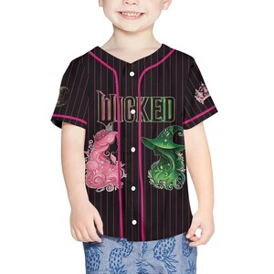 Pu&ograve; includere: Maglia da baseball nera con gessati e dettagli rosa. La parola "WICKED" &egrave; stampata sul petto. Presenta illustrazioni di un personaggio dai capelli rosa con una corona e una strega dai capelli verdi con un cappello. La maglia ha una chiusura con bottoni.