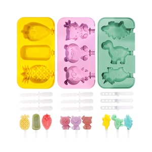 May include: Three silicone popsicle molds with different designs: a pineapple, a pig, and a dinosaur. Each mold has three popsicle slots and comes with six wooden sticks. The molds are yellow, pink, and green.